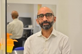 Dr Priyadarshi standing in front of a mirror wearing a white shirt and glasses