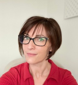 Dr Packard in front of a white wall wearing a red top and black glasses