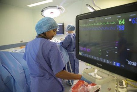 Surgeon standing beside monitor, with patient undergoing surgery in backgorund