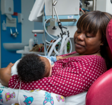 Picture of a mother sitting in a chair in the neonatal unit feeding her baby